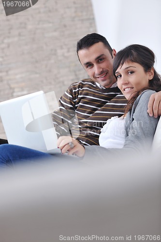 Image of joyful couple relax and work on laptop computer at modern home