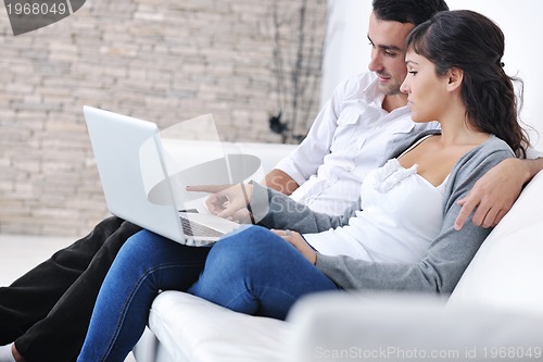 Image of joyful couple relax and work on laptop computer at modern home