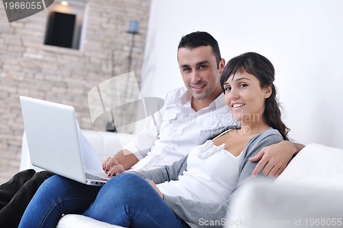 Image of joyful couple relax and work on laptop computer at modern home