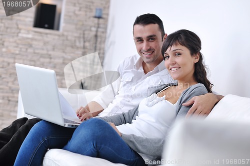 Image of joyful couple relax and work on laptop computer at modern home