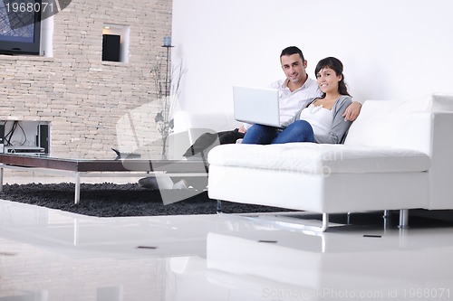 Image of joyful couple relax and work on laptop computer at modern home