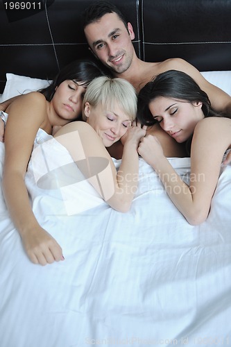 Image of Young handsome man lying in bed with three girls