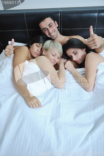 Image of Young handsome man lying in bed with three girls