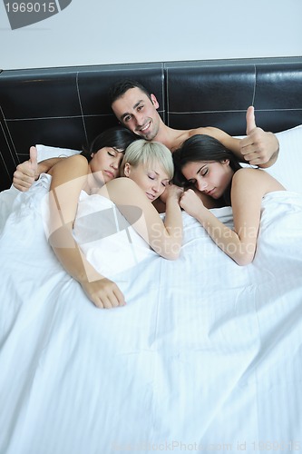 Image of Young handsome man lying in bed with three girls