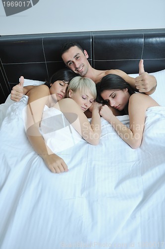 Image of Young handsome man lying in bed with three girls