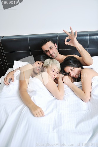 Image of Young handsome man lying in bed with three girls