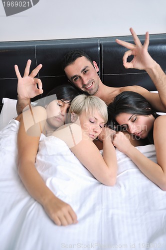 Image of Young handsome man lying in bed with three girls