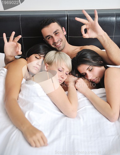 Image of Young handsome man lying in bed with three girls