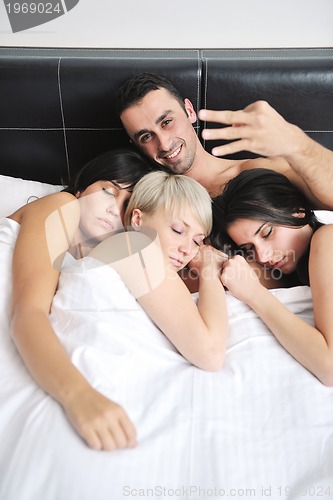 Image of Young handsome man lying in bed with three girls