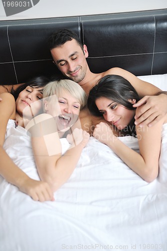 Image of Young handsome man lying in bed with three girls