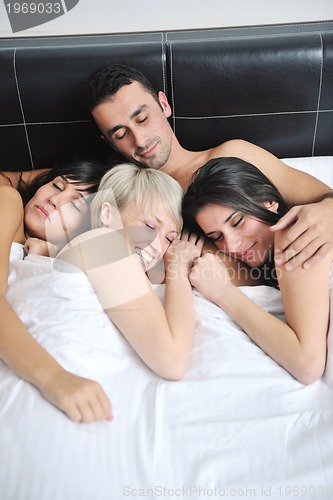 Image of Young handsome man lying in bed with three girls