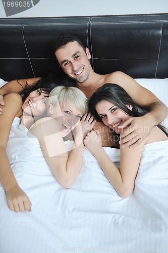 Image of Young handsome man lying in bed with three girls