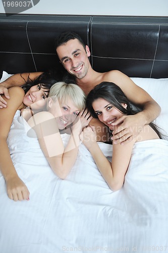 Image of Young handsome man lying in bed with three girls