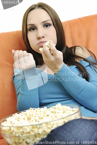 Image of young woman eat popcorn on orange sofa