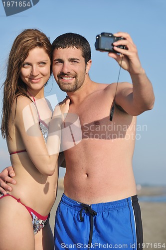 Image of happy young couple in love taking photos on beach