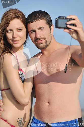 Image of happy young couple in love taking photos on beach