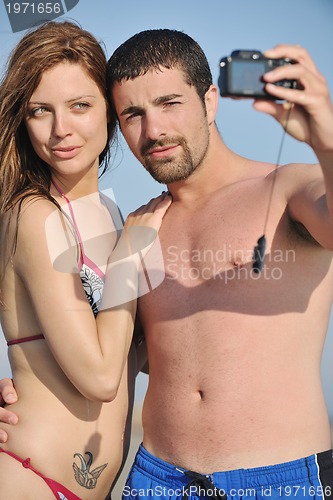 Image of happy young couple in love taking photos on beach