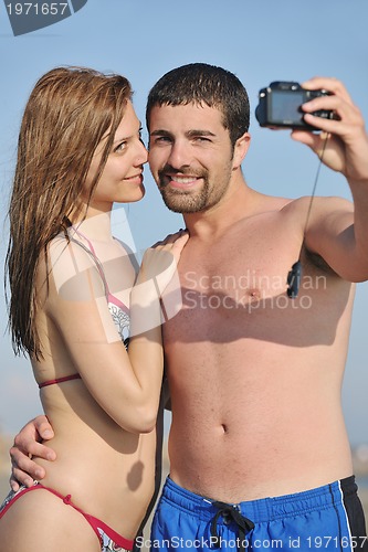 Image of happy young couple in love taking photos on beach
