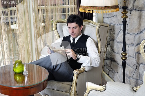 Image of young man reading book and relaxing in luxury indoor