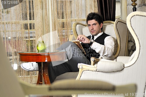 Image of young man reading book and relaxing in luxury indoor