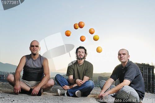 Image of three man outdoor play with orange fruit