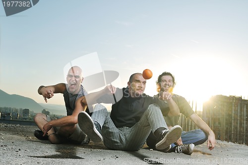 Image of three man outdoor play with orange fruit