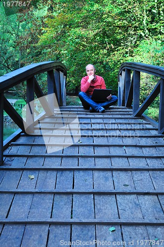 Image of young businessman in red shirt at bridge  working on laptop 