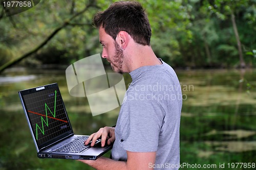 Image of young businessman working on laptop outdoor