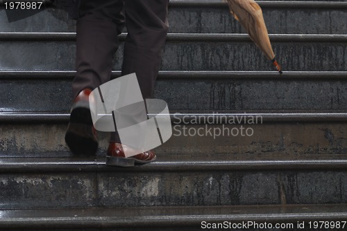 Image of business executive climbing up stairs with umbrela in his hand