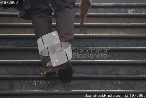 Image of business executive climbing up stairs with umbrela in his hand