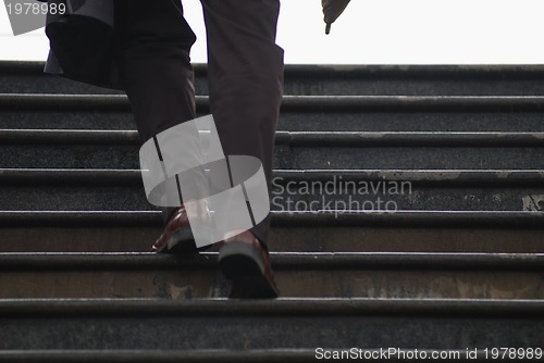 Image of business executive climbing up stairs with umbrela in his hand