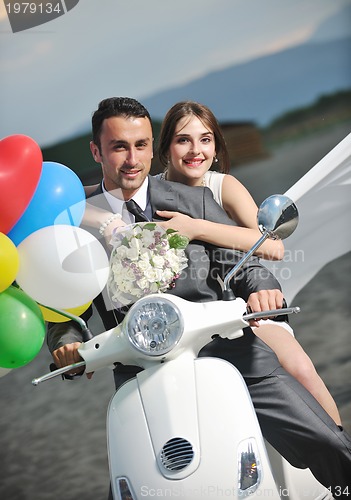 Image of just married couple on the beach ride white scooter