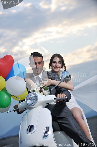 Image of just married couple on the beach ride white scooter