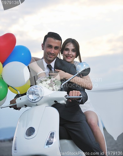 Image of just married couple on the beach ride white scooter