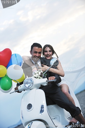 Image of just married couple on the beach ride white scooter