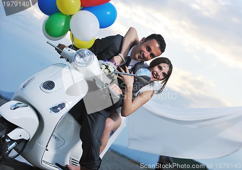 Image of just married couple on the beach ride white scooter