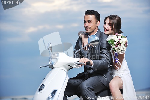 Image of just married couple on the beach ride white scooter