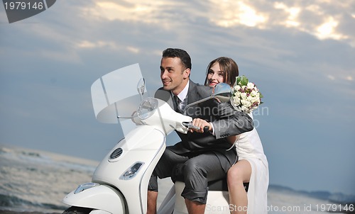 Image of just married couple on the beach ride white scooter