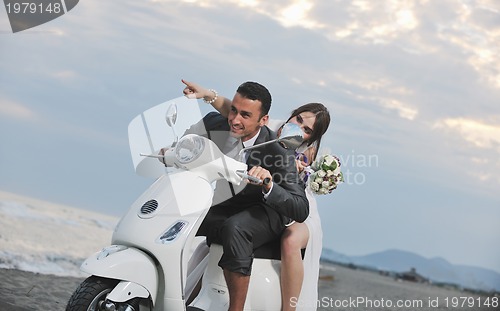 Image of just married couple on the beach ride white scooter