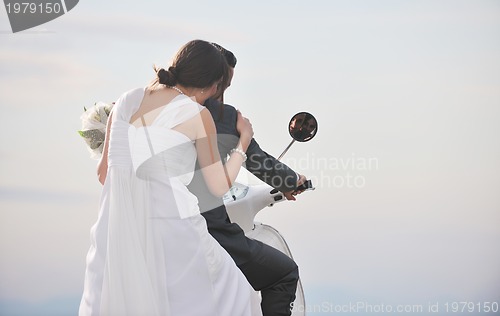 Image of just married couple on the beach ride white scooter