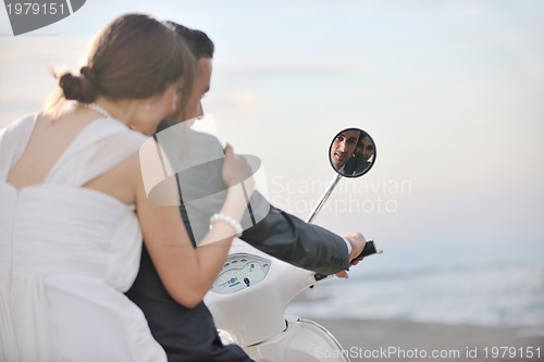 Image of just married couple on the beach ride white scooter