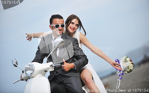 Image of just married couple on the beach ride white scooter