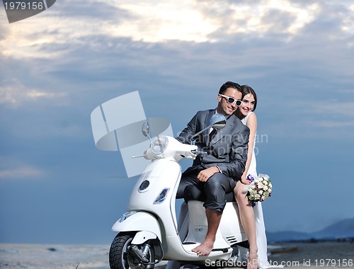 Image of just married couple on the beach ride white scooter