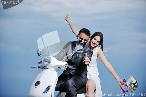 Image of just married couple on the beach ride white scooter