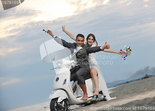 Image of just married couple on the beach ride white scooter