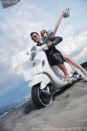 Image of just married couple on the beach ride white scooter