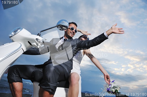 Image of just married couple on the beach ride white scooter