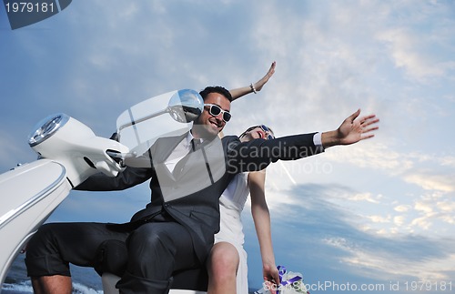 Image of just married couple on the beach ride white scooter