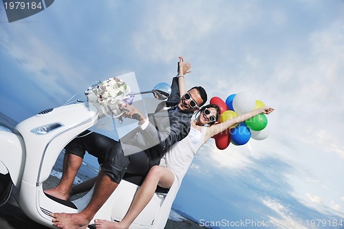 Image of just married couple on the beach ride white scooter