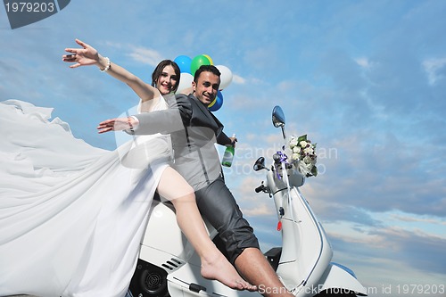 Image of just married couple on the beach ride white scooter